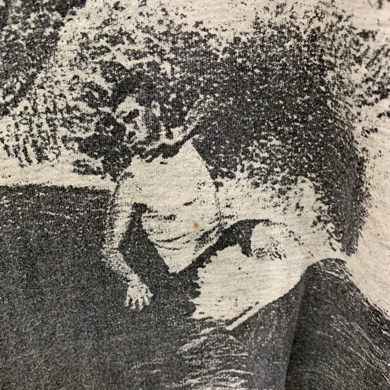 May include: A black and white graphic print of a person surfing on a wave. The print is on a gray t-shirt.