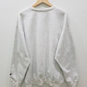 May include: A grey sweatshirt with a crew neck and long sleeves. The sweatshirt has a small logo on the left sleeve.