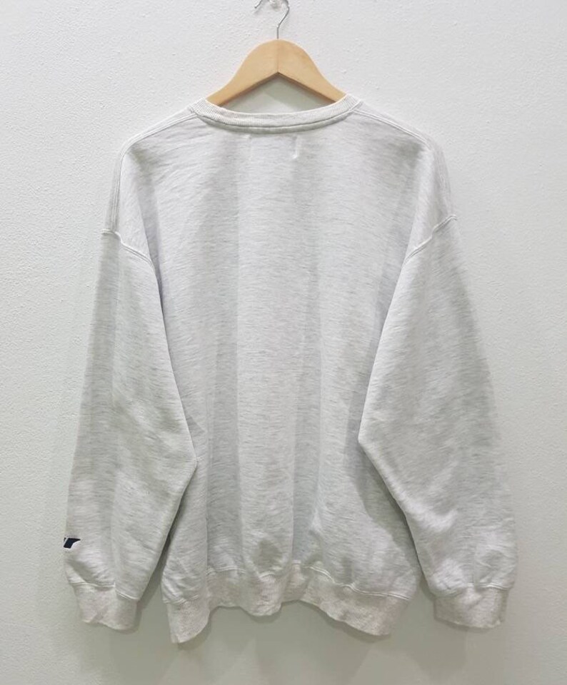 May include: A grey sweatshirt with a crew neck and long sleeves. The sweatshirt has a small logo on the left sleeve.