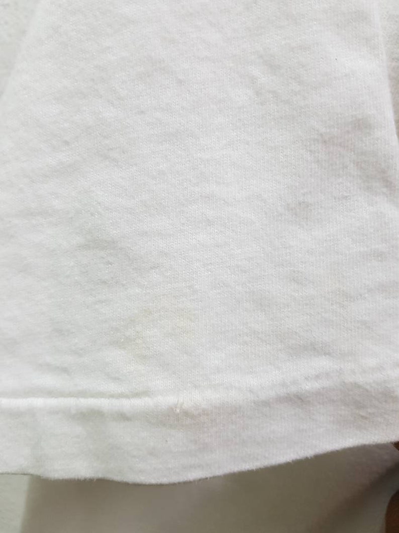 Puede incluir: Primer plano de una camiseta de algod&oacute;n blanco lisa. La tela tiene una textura suave y un aspecto ligeramente acanalado.
