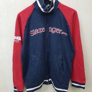 May include: A blue and red zip-up jacket with white trim. The jacket has the words "Slazenger" in red on the front. The jacket also has a white logo with the word "Record" on the left sleeve.