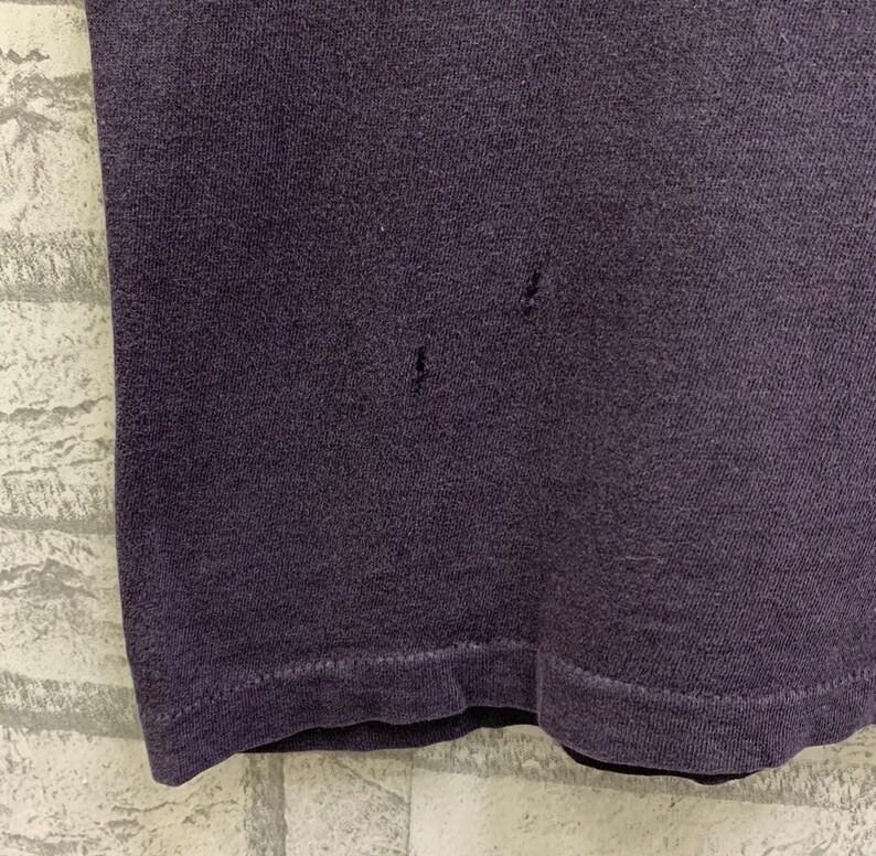 May include: A close-up of a dark purple t-shirt with a few small holes in the fabric.