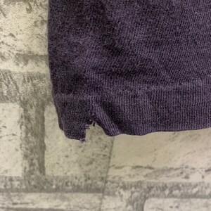 May include: Close-up of the bottom edge of a dark purple t-shirt. The fabric is soft and has a slight texture. The edge of the shirt is frayed.