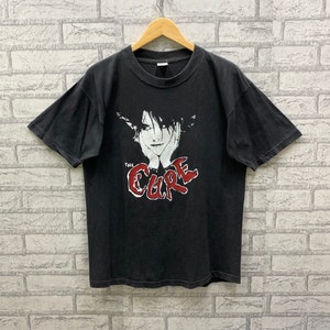 May include: Black t-shirt with a white and red graphic of a person's face and the text "The Cure".