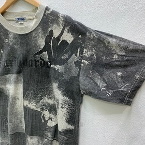 May include: Gray t-shirt with a faded print of skateboarders and waves. The shirt has a crew neck and short sleeves. The text "CALI-JA" is visible on the tag.