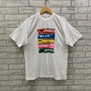 Puede incluir: Camiseta blanca con un gráfico colorido de los personajes de Power Rangers. El gráfico presenta los nombres de cada ranger y su color correspondiente: rojo, azul, amarillo, rosa y verde.