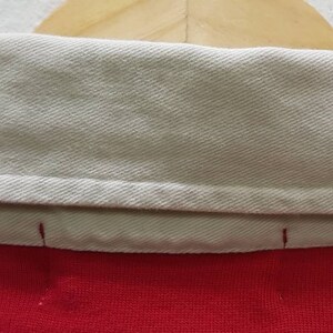 May include: Close-up of the inside of a red and white collared shirt. The collar is folded down and the white fabric is visible.