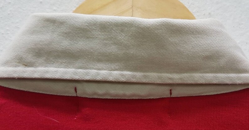 May include: Close-up of the inside of a red and white collared shirt. The collar is folded down and the white fabric is visible.