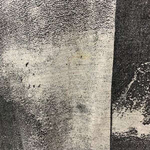 May include: Close-up of a black and white patterned fabric with a faded, white area. The fabric has a textured, woven appearance.