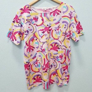 May include: A pink short-sleeved t-shirt with a colorful abstract print featuring palm trees, circles, and geometric shapes in shades of pink, yellow, blue, and purple.