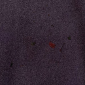 May include: A close-up of a dark purple fabric with several small, faded stains in shades of red, green, and brown.