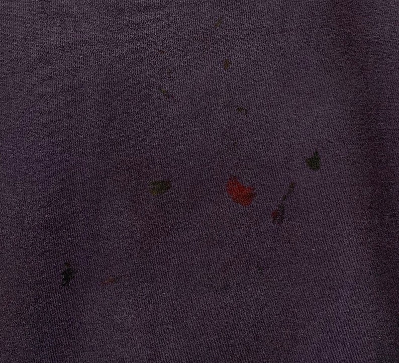 May include: A close-up of a dark purple fabric with several small, faded stains in shades of red, green, and brown.