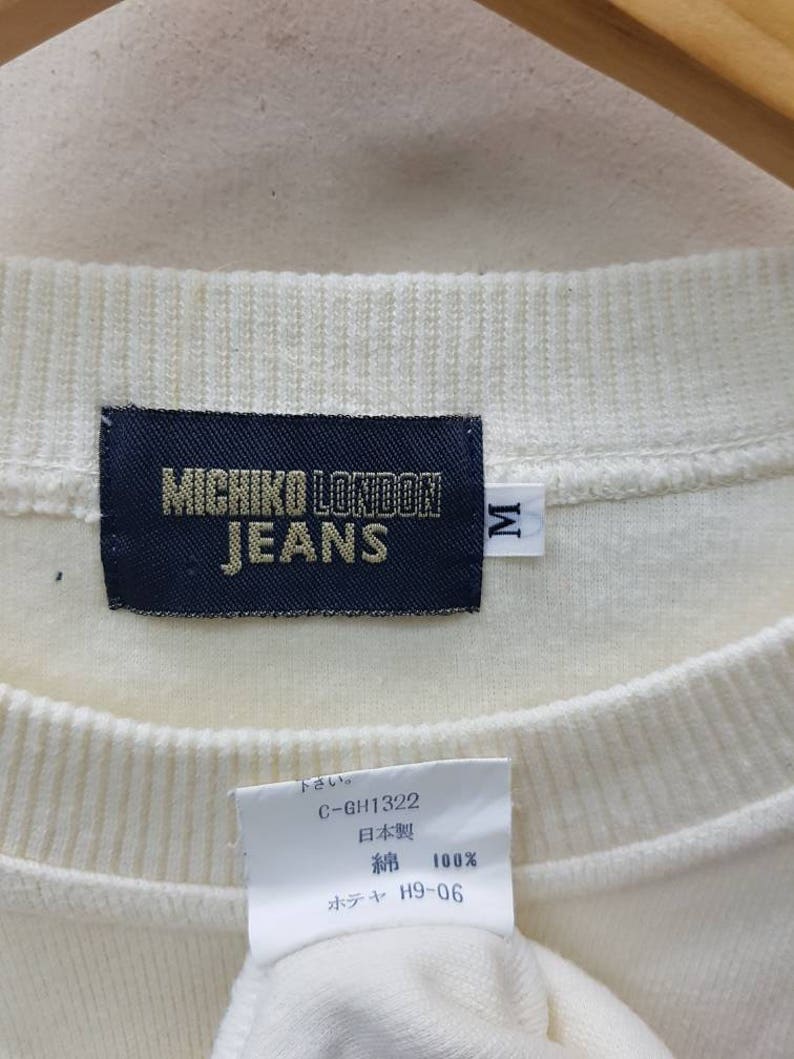 May include: White cotton sweatshirt with a black label that reads "MICHIKO LONDON JEANS" and a size tag that reads "M". The label also includes the text "C-GH1322", "日本製" (Japanese for "Made in Japan"), "綿 100%" (Japanese for "100% cotton"), and "ホテャ H9-06".