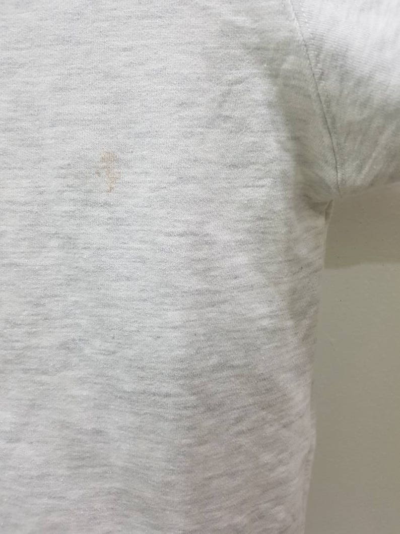 May include: A close-up of a light grey t-shirt with a small brown stain.