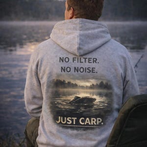May include: A light gray hoodie with the text "NO FILTER. NO NOISE. JUST CARP." printed on the back. The graphic depicts a carp in a lake. The person is sitting near a body of water.