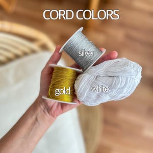 May include: Three spools of cord in gold, silver, and white. The spools are labeled with the corresponding colors. CORD COLORS is written above the spools.