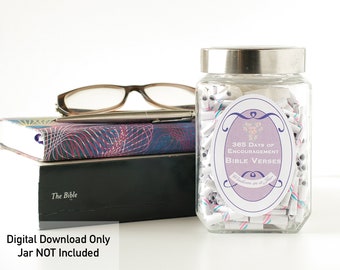 May include: A glass jar filled with rolled up pieces of paper with pink and blue stripes. The jar has a silver lid and a label that reads "365 Days of Encouragement Bible Verses Wisdom in a Jar".