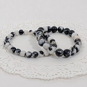 Peut inclure: Deux bracelets en perles à motifs noirs et blancs. Les bracelets sont empilés l'un sur l'autre.