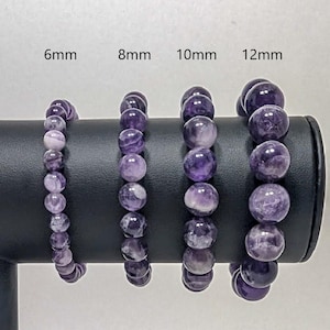 May include: Four amethyst gemstone bracelets displayed on a black stand. The bracelets are shown in four different sizes: 6mm, 8mm, 10mm, and 12mm.