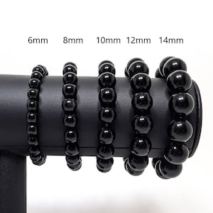 May include: Five black beaded bracelets of different sizes, displayed on a black stand. The bracelets are labeled with their bead size in millimeters: 6mm, 8mm, 10mm, 12mm, and 14mm.