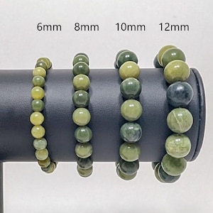 May include: Four beaded bracelets with varying bead sizes (6mm, 8mm, 10mm, and 12mm) are displayed. The beads are primarily shades of green, with some variation in color. The bracelets are presented on a black display stand against a white background.