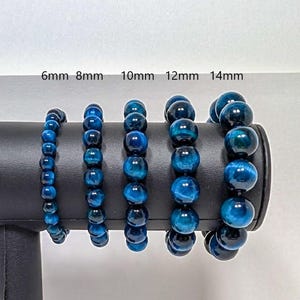 May include: Five blue gemstone bracelets of varying sizes, displayed on a black stand. The bracelets are labelled 6mm, 8mm, 10mm, 12mm, and 14mm.