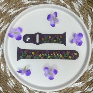 May include: A brown Apple Watch band with a floral design. The band has a variety of colorful flowers, including red, yellow, green, and purple.