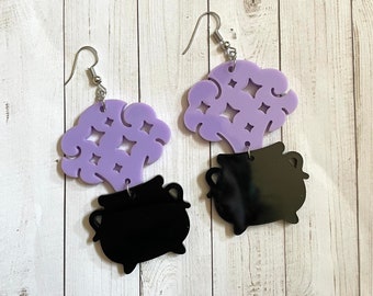 May include: A pair of purple and black earrings featuring a cauldron with a purple cloud of smoke and stars coming out of the top.