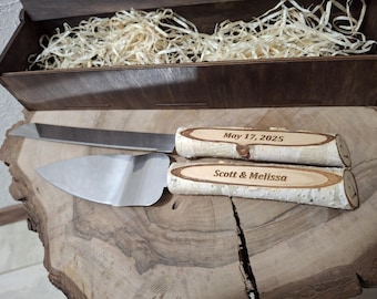 May include: A wedding cake knife and server set with birch bark handles. The knife blade is serrated, and the server is triangular. The handles are engraved with "May 17, 2025" and "Scott & Melissa". The set is displayed on a wooden surface.