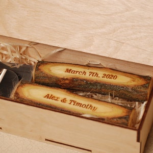 May include: A wooden box with its lid open, showing two wooden cake servers with engraved text. The top server reads "March 7th. 2020" and the bottom server reads "Alex & Timothy".