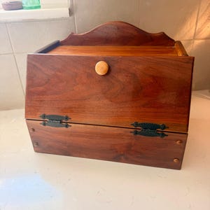 May include: A wooden box with a hinged front door and a curved top. The box is stained a rich brown color and has a small wooden knob. The hinges are black. The box is likely used for storage.