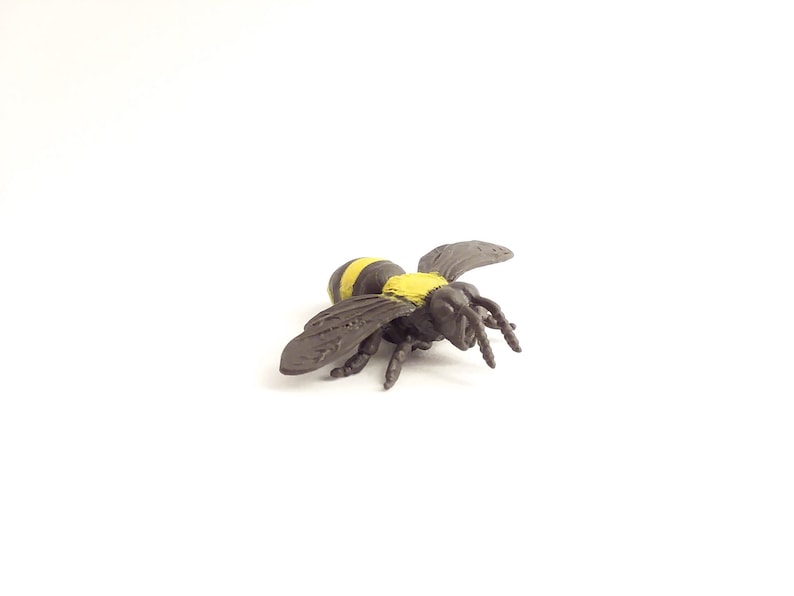 May include: A black and yellow plastic bee toy. The bee has black wings and yellow stripes on its body.