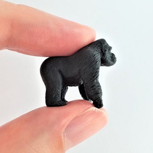 May include: A small black gorilla figurine, standing on two legs, with its arms at its sides. The figurine is about 2 inches tall.