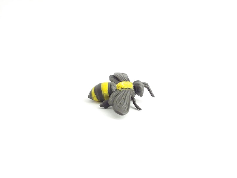 May include: A black and yellow plastic bee toy. The bee has black wings and yellow stripes on its body.