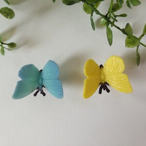 Peut inclure: Deux pinces &agrave; cheveux en forme de papillon en plastique, l'une bleue et l'autre jaune.