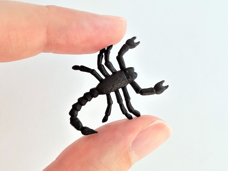 Puede incluir: Una figura de escorpi&oacute;n de pl&aacute;stico negro. El escorpi&oacute;n est&aacute; en posici&oacute;n con la cola levantada y las garras extendidas.