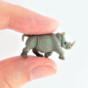 May include: A small gray plastic rhinoceros figurine. The rhino is standing on its four legs with its head held high.
