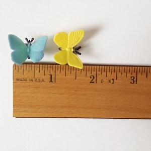 Peut inclure: Deux papillons en plastique, l'un bleu et l'autre jaune, sont plac&eacute;s sur une r&egrave;gle en bois. La r&egrave;gle est gradu&eacute;e en pouces et porte la mention "MADE IN U.S.A."