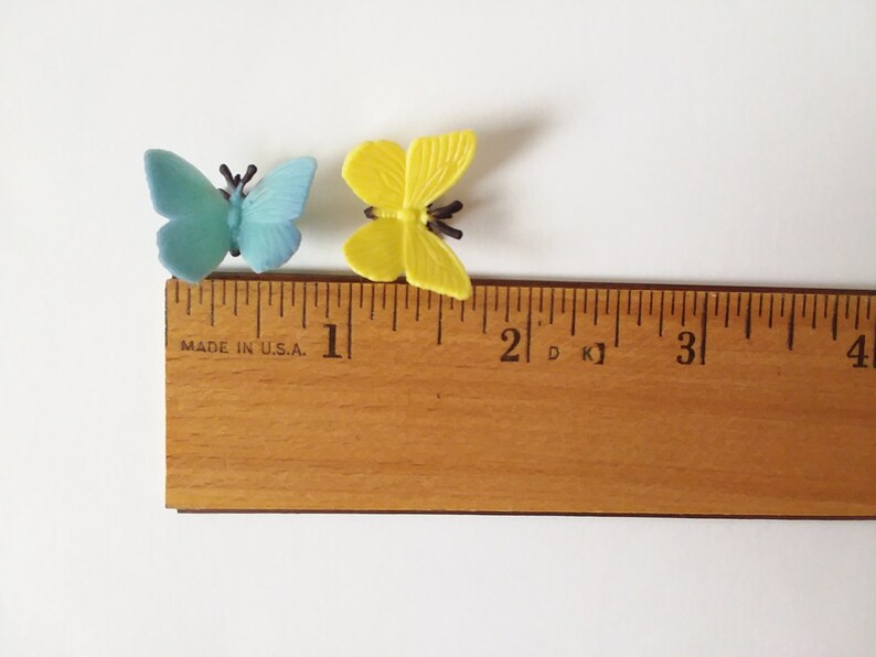 Peut inclure: Deux papillons en plastique, l'un bleu et l'autre jaune, sont plac&eacute;s sur une r&egrave;gle en bois. La r&egrave;gle est gradu&eacute;e en pouces et porte la mention "MADE IN U.S.A."