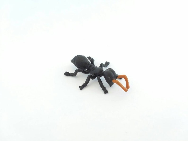 May include: A black plastic ant toy with orange antennae and legs. The ant is positioned on a white background, showcasing its detailed features. The toy is a miniature replica of an ant.