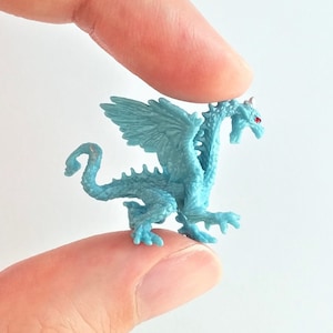 May include: A small, blue plastic dragon figurine with red eyes and wings. The dragon is posed in a standing position with its wings spread out.