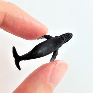 May include: A small black plastic figurine of a humpback whale. The whale is posed in a swimming position with its tail raised.