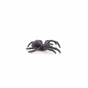 May include: A black plastic spider toy with eight legs. The spider is lying on its back with its legs spread out.