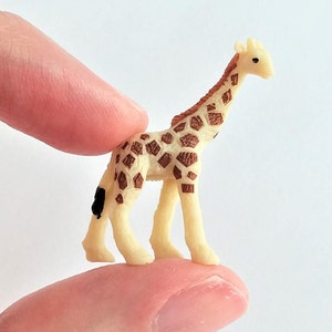 May include: A small, cream-colored plastic giraffe figurine with brown spots. The giraffe is standing on its four legs with its head held high.