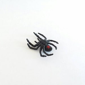 May include: Black plastic toy spider with a red hourglass marking on its abdomen.