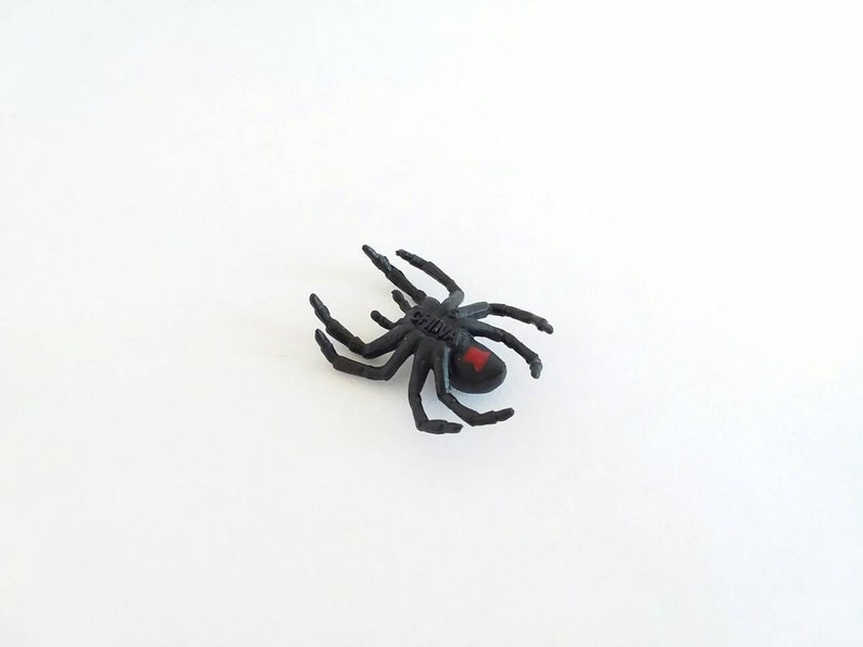 May include: Black plastic toy spider with a red hourglass marking on its abdomen.