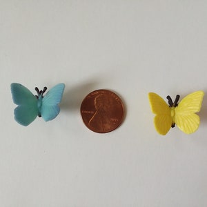 Peut inclure: Deux petits papillons en plastique, l'un bleu et l'autre jaune, sont repr&eacute;sent&eacute;s &agrave; c&ocirc;t&eacute; d'un penny am&eacute;ricain. Les papillons sont &agrave; peu pr&egrave;s de la taille d'un penny.
