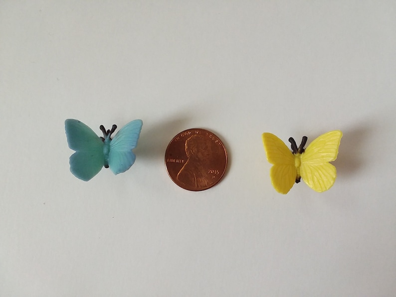 Peut inclure: Deux petits papillons en plastique, l'un bleu et l'autre jaune, sont repr&eacute;sent&eacute;s &agrave; c&ocirc;t&eacute; d'un penny am&eacute;ricain. Les papillons sont &agrave; peu pr&egrave;s de la taille d'un penny.