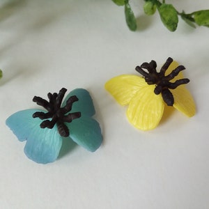 Peut inclure: Deux figurines de papillons en plastique avec des antennes noires. Un papillon est bleu et l'autre est jaune.