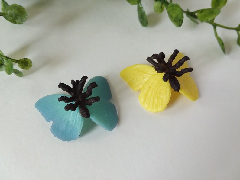 Peut inclure: Deux figurines de papillons en plastique avec des antennes noires. Un papillon est bleu et l'autre est jaune.